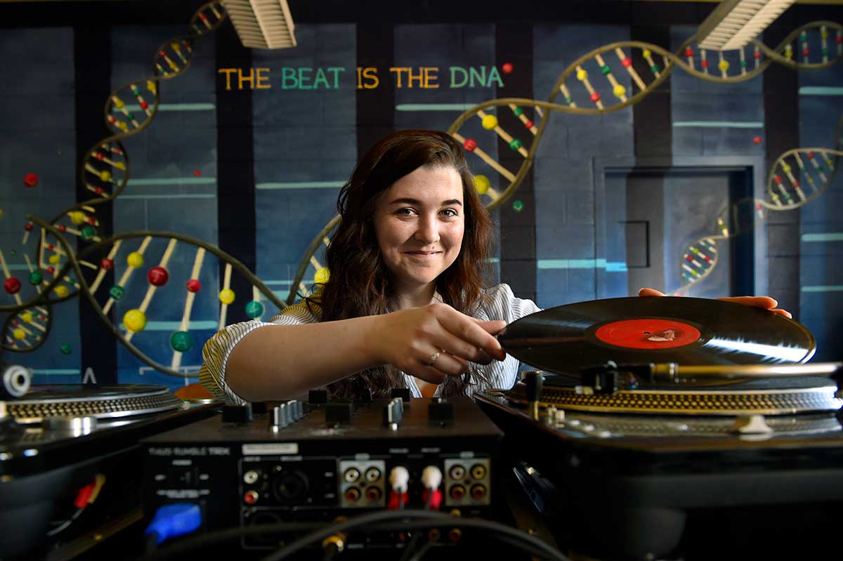 Emily Hynes puts a record on a record player in a recording studio.
