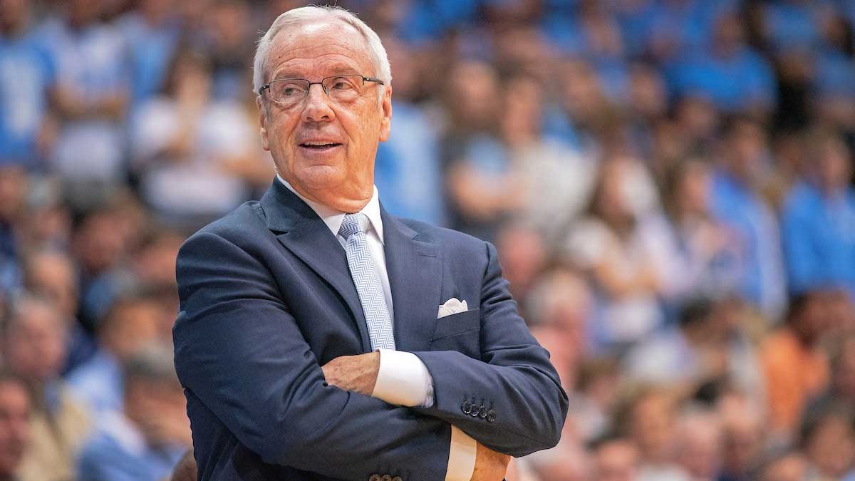 Head Coach Roy Williams stands with arms crossed at a basketball game.