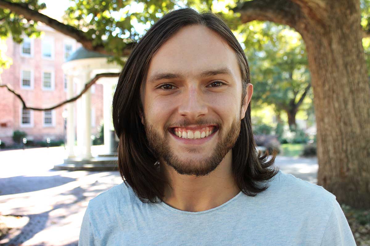 A closeup portrait of Carolina student Elijah Watson with the Old Well in the background.