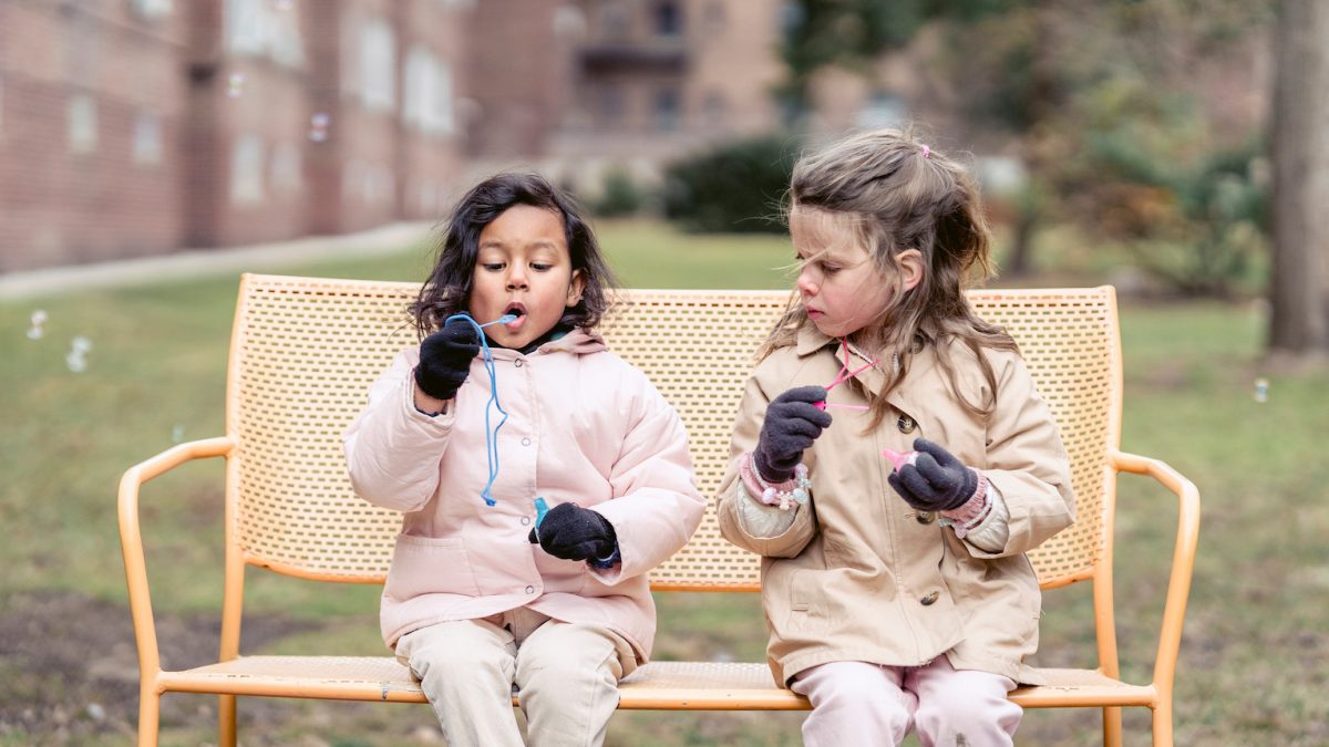 Two girls on a park bench blowing bubbles