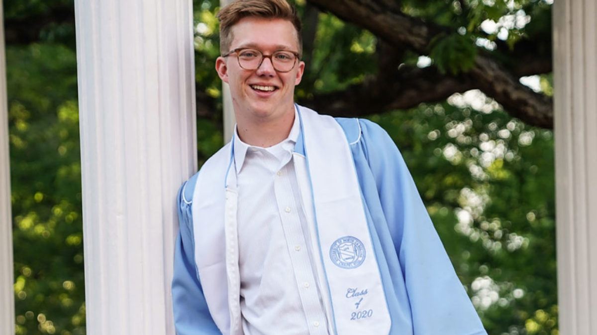 Cole Mueller poses in front of the Old Well in a cap and gown
