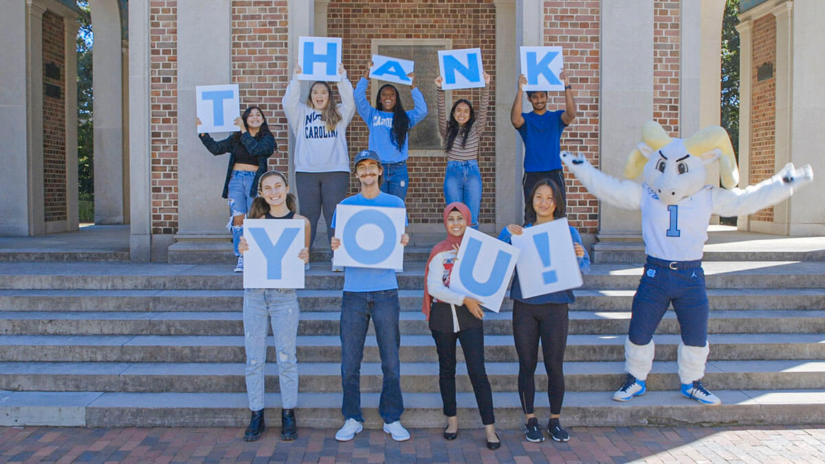 Carolina students standing in front of the Bell Tower while holding up cards that spell Thank you!
