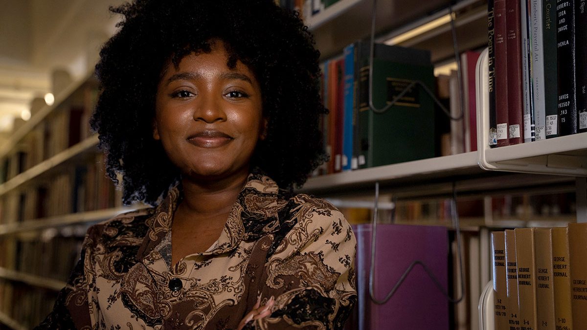 A portrait of Ayana Monro in a library in front of books.