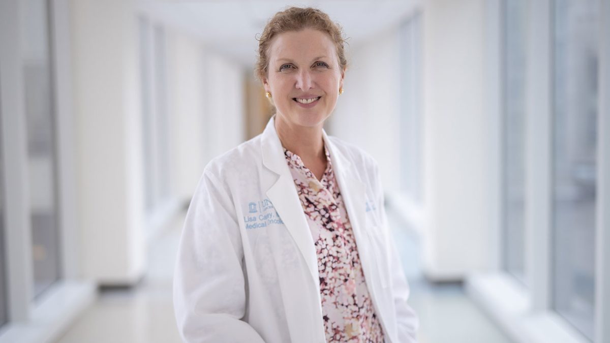 Dr. Lisa Carey wears a white lab coat and poses in a hospital hallway.
