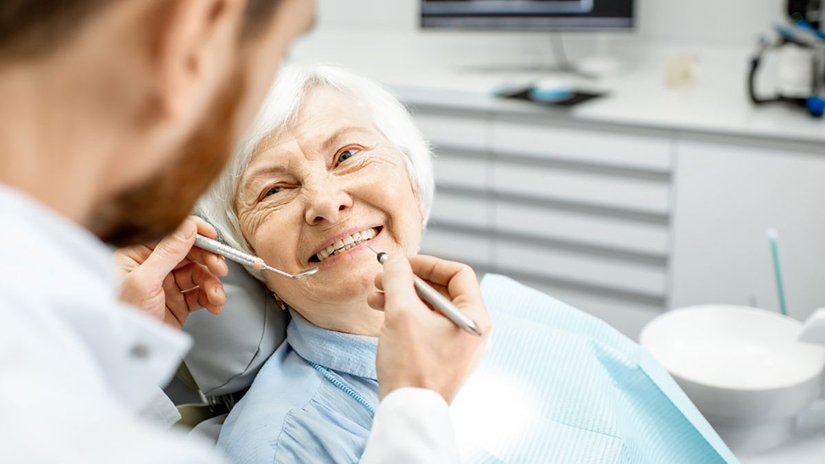 Dentist holding tools close to elderly female patient's teeth