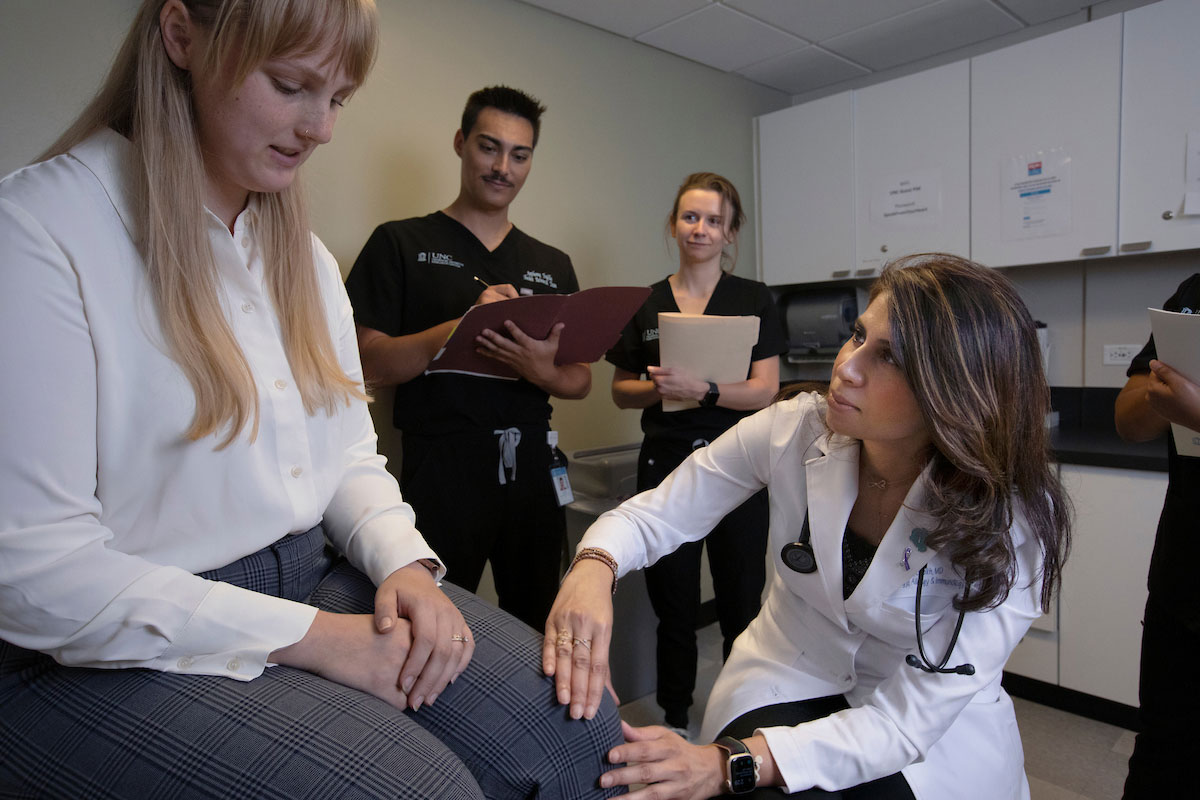 Dr. Sheikh examines a patient with health care professionals taking notes in the background.