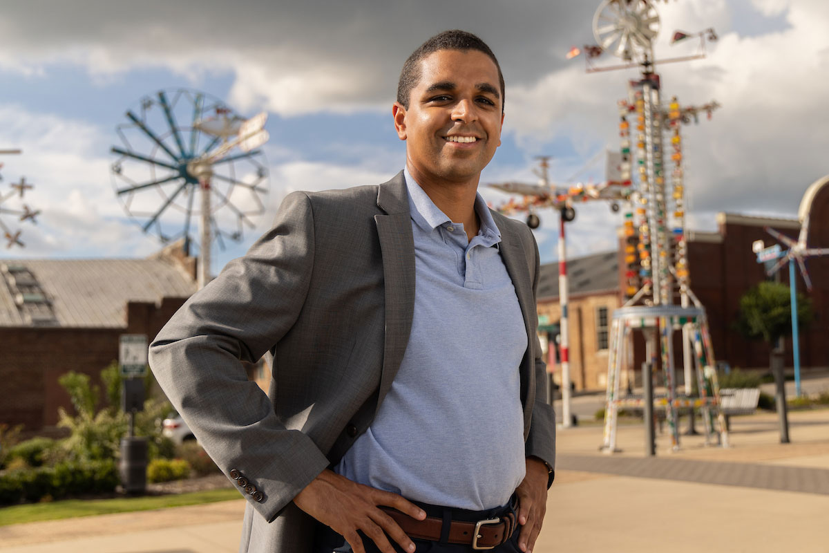 Dante Pittman poses outside with hands on hips and whirligigs in the background.