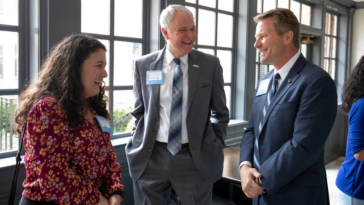 Ana Zurita Posas, Scott Hamilton, and Kevin Guskiewicz stand laughing at the Golden LEAF Luncheon