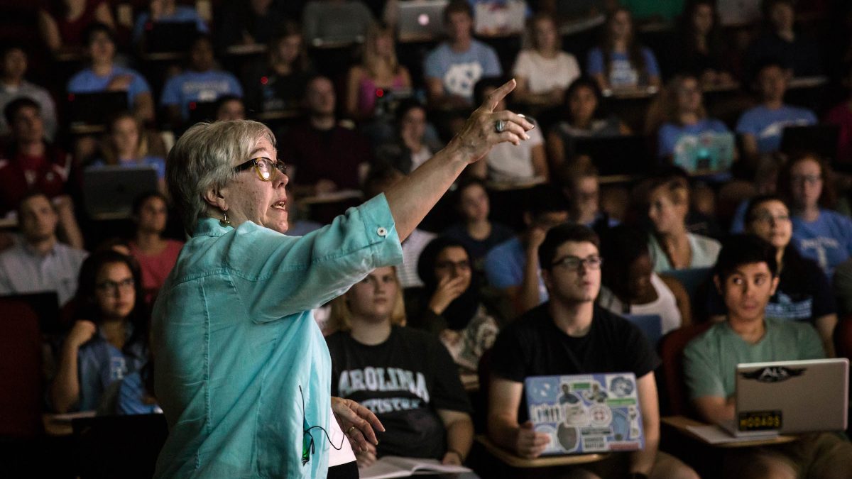 Professor pointing at a screen in front of a large lecture class of students