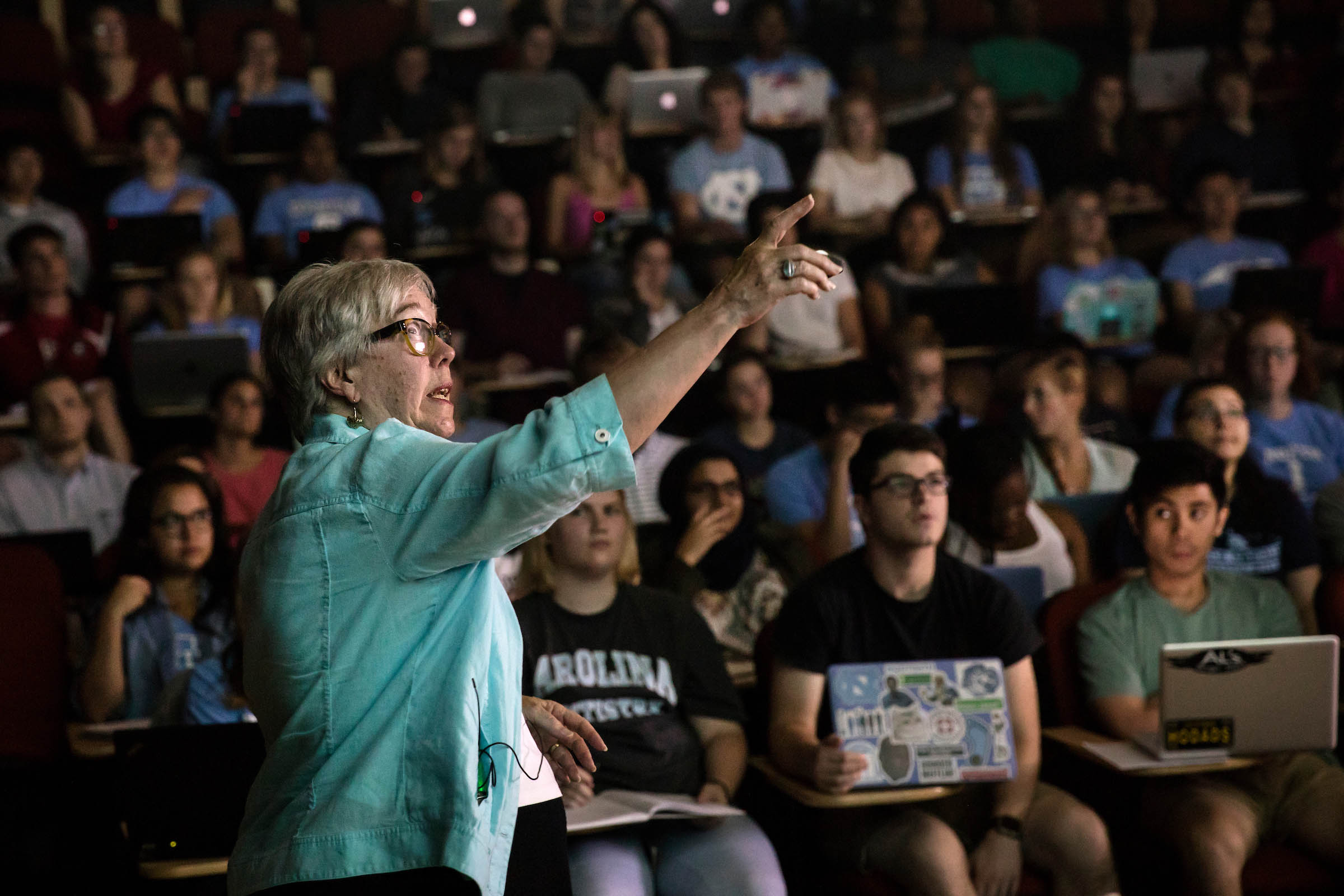 Professor pointing at a screen in front of a large lecture class of students